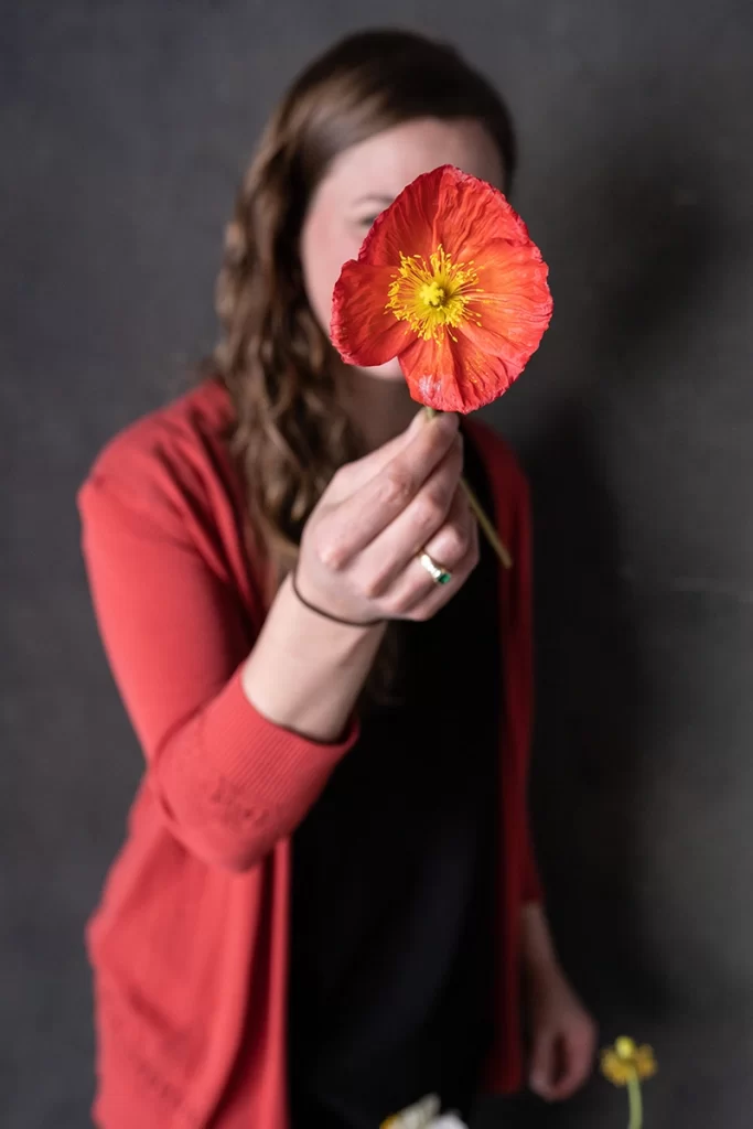 brunette-woman-holding-up-red-and-yellow-flower-to-hide-her-face-from-camera