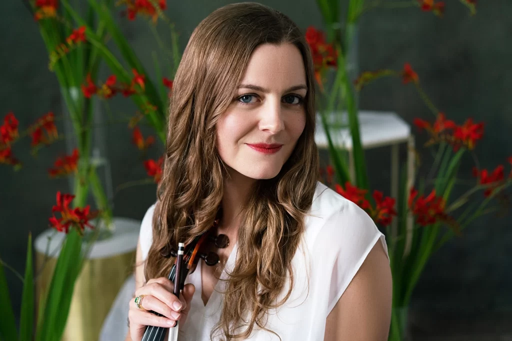 close-up-of-woman-holding-her-violin-with-red-flowers-in-background