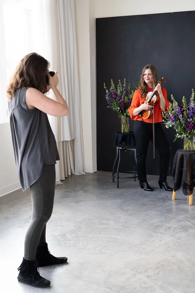 photo-of-rachel-taking-picture-of-woman-holding-her-violin-in-front-of-black-background-with-flowers