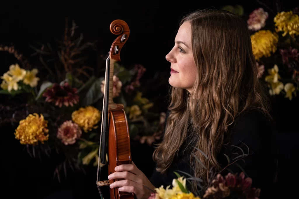 profile-of-brunette-woman-holding-her-violin-with-yellow-pink-and-maroon-flowers-in-background