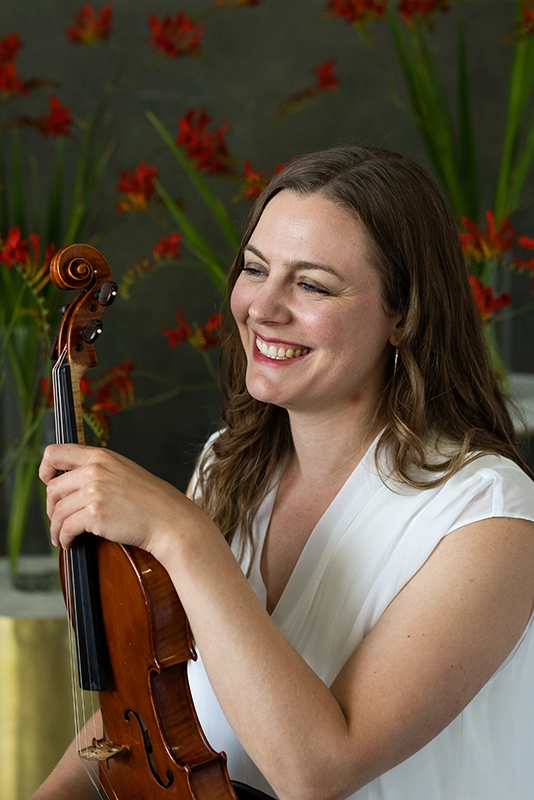 profile-of-woman-smiling-with-her-violin-in-hand-in-front-of-red-flowers