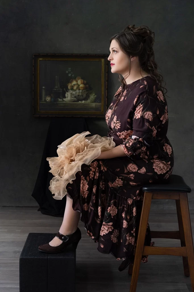 white-woman-in-floral-dress-sitting-in-front-of-painting