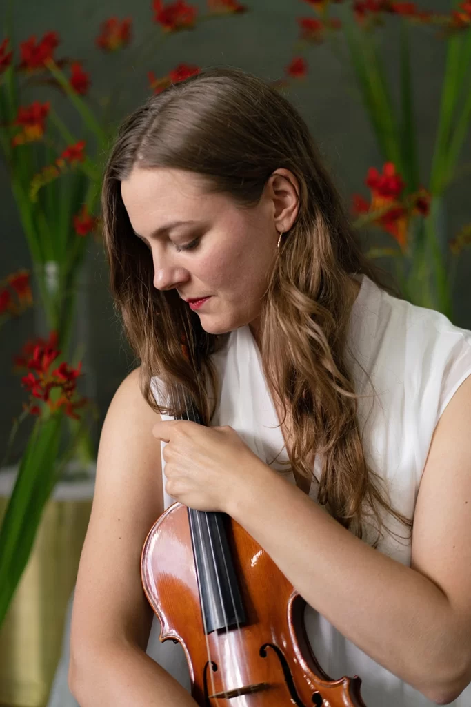 woman-holding-violin-and-looking-down-with-red-flowers-in-background