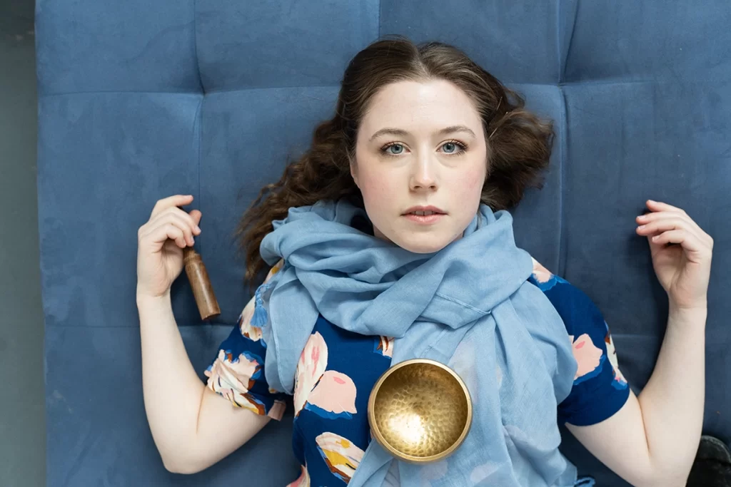 woman-laying-down-on-blue-couch-with-brass-singing-bowl
