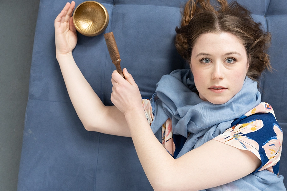 woman-laying-on-blue-couch-looking-at-the-camera-while-posing-with-brass-singing-bowl