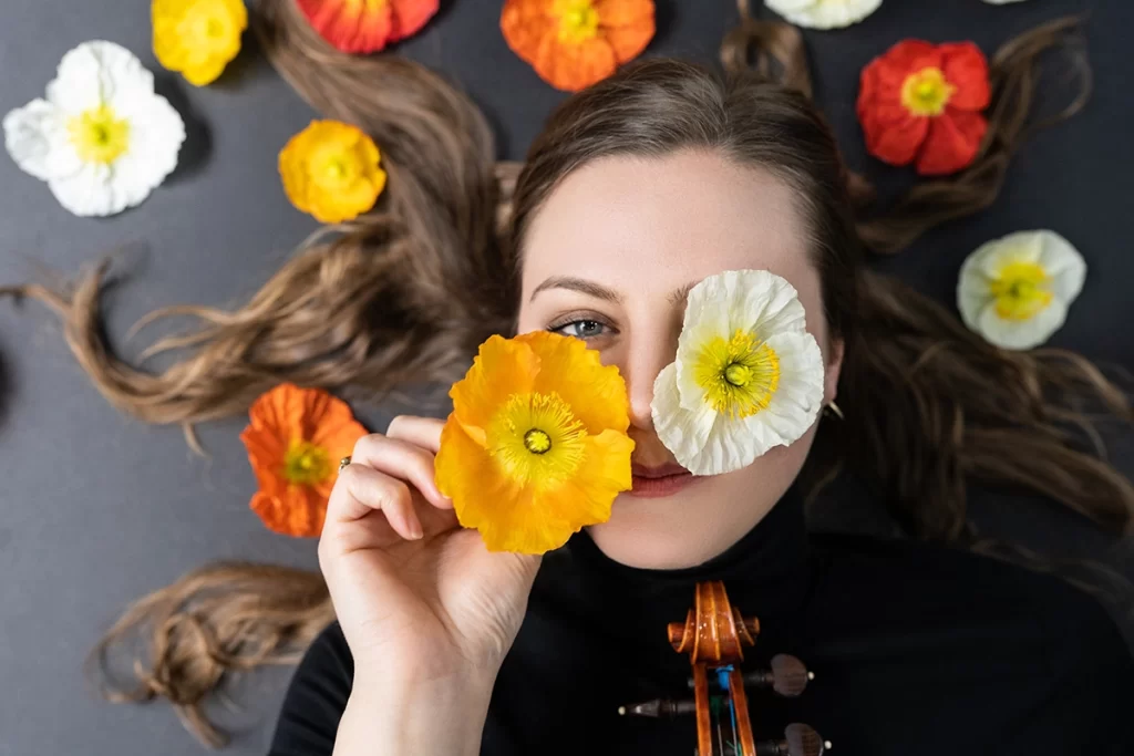 woman-lying-on-the-ground-with-yellow-white-and-orange-flowers-around-her-head-and-two-flowers-on-her-face