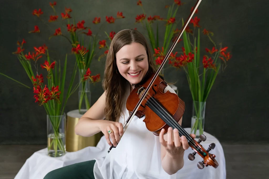 woman-smiling-while-playing-violin-with-red-flowers-in-background