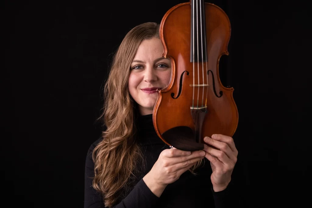 woman-wearing-all-black-holding-up-violin-to-side-of-her-face-smiling