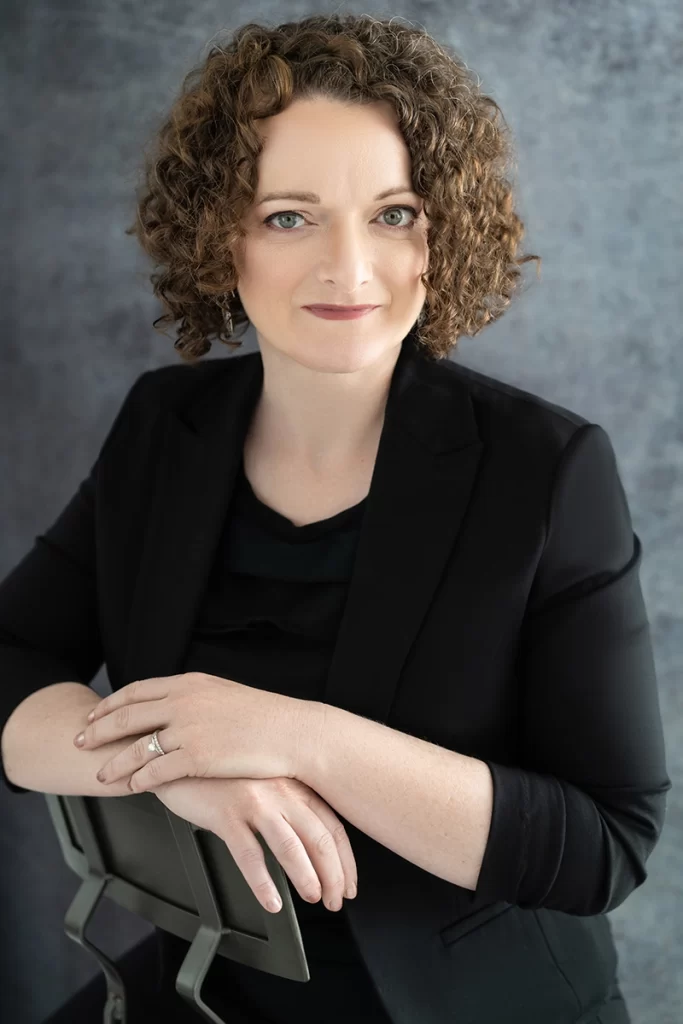 woman-with-short-curly-brown-hair-in-business-attire-leaning-on-chair-back