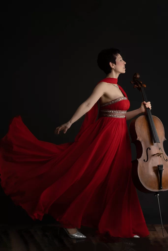 woman-in-red-flowy-dress-holding-cello-while-dress-trails-behind-her